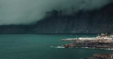 Ağır gri bulutlar karanlık okyanusta büyük kayaları kapladı. Fırtınadan önce hava. Craggy volkanik adası Tenerife, Los Gigantes uçurumları, Kanarya İspanya. Deniz manzarası üzerinde kasvetli bir gökyüzü.