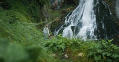 Avusturya dağlarında şelalenin tadını çıkaran bir kadın gezgin. Dağlarda seyahat, macera ve gezi konsepti. Kız ormandaki doğanın güzelliğini düşünüyor..
