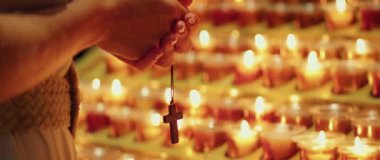 Kilisede dua eden bir kadın. Yetişkin bir kız yanan mumların yanında haçla el ele tutuşuyor. Doğal ateş ışığı.