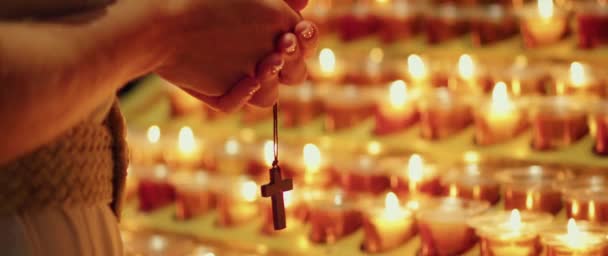 教会で祈っている女性 燃えるろうそくの近くで十字架で手を握る大人の少女 ナチュラルファイアライト — ストック動画