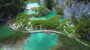 Gölün berrak zümrüt suyu üzerindeki ahşap dar köprünün inanılmaz manzarası. Manzaralı şelalelerle dağ ulusal parkında yürüyüş yapmak. Plitvice Lakes Ulusal Parkı Hırvatistan. Seyahat ve doğa