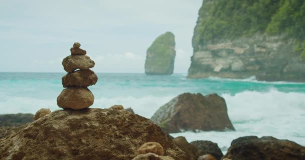 瞑想のための石の禅ピラミッド ビーチでバランスをとるロックタワー 海のターコイズ水 海の波が飛び散る海の景色 セレニティー ハーモニー 落ち着き コンセプト — ストック動画