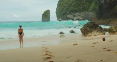 Mutlu kadın kumlu sahilde büyük okyanus dalgalarından kaçarak koşuyor. Siyah mayo giymiş gülümseyen turist kız deniz kıyısında iyi eğlenceler. Tembeling Bali, Nusa Penida, Endonezya.