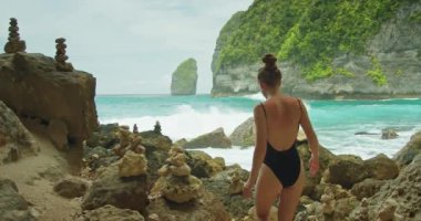 Endonezya 'nın Nusa Penida tropikal adası kayalıkları yakınlarındaki Tembeling plajı, Bali' nin kayalık kıyılarıyla çarpışan kadın, okyanus dalgalarının güçlü spreyini gözlemler..