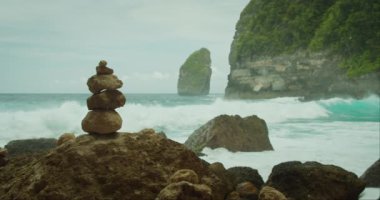 Taşlardan oluşan bir cairn, Tembeling Sahili 'ndeki çalkantılı denize karşı mükemmel bir şekilde dengede duruyor. Arka planda Nusa Penida. Dalgaları parçalamak, doğanın gücü ve barışı. Sakin sahne.