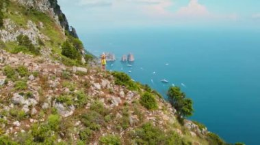 Kadın, Rocky Summit 'ten Capris Faraglioni' yi izliyor. Yaz kıyafetleri içindeki turistler, deniz sularındaki deniz gemilerini inceliyor. İtalyan bayramı..