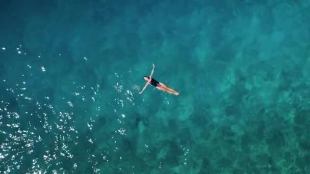 女孩在水晶清澈的海水中游泳 一个游泳者的轮廓被巧妙地投射在阳光照射下的水上挂毯上 一种排斥性的感觉 — 图库视频影像