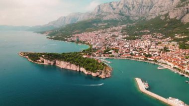 Makarska Riviera 'nın bereketli yeşil dağ zeminli sahil cazibesi. Açık yaz gökyüzünün altında manzaralı bir kıyı şeridi ve şehir uyumu...