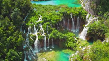 Su ve şelale dereleri olan dağ manzarası. Göl suyunun büyüleyici yeşil rengi. Hırvatistan 'daki Plitvice Gölleri Ulusal Parkı' nda insanlar dar yolda yürüyüş yapıyor. Seyahat ve doğa kavramı.