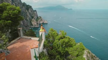 Alacakaranlıkta Capri sahil kayalıkları üzerinde bir balkonda meditasyon yapan biri. İtalya 'da yaz deniz manzarasına karşı kadın duruşu.