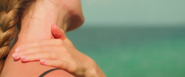 女人在肩上轻柔地涂上抹布霜 做一个自我照顾的姿势 以海洋为背景 把涂防晒霜作为海滩日常活动的一个必要组成部分 — 图库视频影像