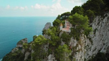 Rahat ve düşünceli bir kadın terasta oturup güneşli bir yaz gününde Capri deniz manzarasının tadını çıkarıyor...
