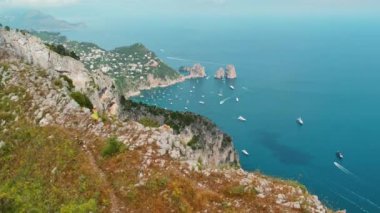 Mavi denizi noktalayan teknelerle Capri Adası 'nın havadan görünüşü. Elbiseli neşeli kız, yüksek bir uçurumun yamacında koşuyor. Okyanusa karşı, Faraglioni kayalarıyla...