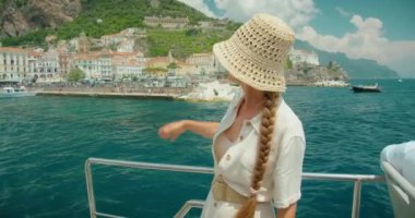 Gök mavisi denizdeki yattan Positano 'ya el sallayan kadın. Manzaralı bir İtalyan sahil şeridinin büyüleyici güzelliğini yaşayan bir turist..