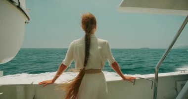 Bir kadın, kıç taraftaki bir teknede, açık bir günde ufku seyrediyor. Parlak güneş ışığı ve derin mavi su ve gökyüzü..