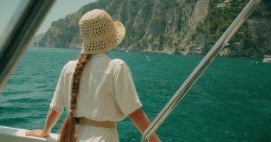 Hasır şapkalı kadın kıyı kasabası Positano 'ya bakıyor. İtalyan Riviera cazibesinin keyfini çıkaran turist köpüklü suya karşı..