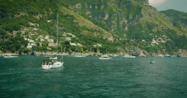 Bir yelkenli, yaz boyunca Positano kayalıklarının kenarındaki sakin sularda yüzer. İtalyan kıyılarıyla deniz eğlencesi manzarası büyüleyicidir...