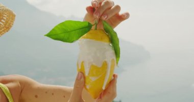 Gülümseyen bir kadının tuttuğu dondurmalı limonun yakın çekimi. Parlak yaz güneşi sahneyi doğal ve sıcak bir ışıkla aydınlatıyor...