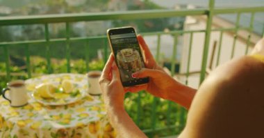 Bir insan kahvaltı sahnesini akıllı telefondan yakalar. İngiliz çayı ve limonlu iki fincan. Ilık sabah ışığı, balkonda sıcak bir ışıltıyla yıkanır...