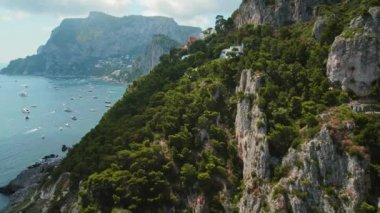Yeşillik, Capri 'nin denize bakan uçurumlarını süslüyor. Yazın güneşli bir günde yüzen yatları ve tekneleri olan bir sahil. İtalya..