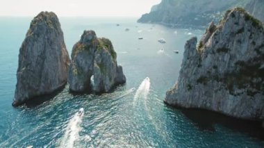 Tekneler yazın Capri Adası 'ndaki görkemli Faraglioni deniz yığınları etrafındaki sakin deniz sularında yol alırlar. Keyif yatlarıyla deniz manzarası..
