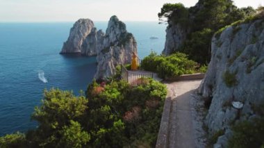 Sarı elbiseli bir kadın, Capri manzaralı Faraglioni 'ye, doğanın güzelliğiyle çevrili, uçurum kenarından hayran...