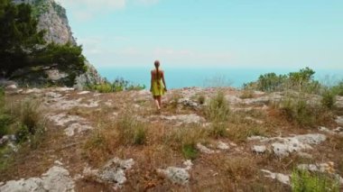 Capri kayalıklarında yürüyüş yapan bir kadın, Tyrhenian Denizi 'nin ihtişamına bakıyor. Görkemli üç kaya oluşumu Faraglioni..