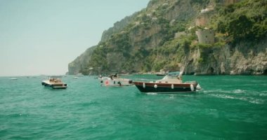 Güneşli bir yaz günü, İtalya 'nın Amalfi Sahili' nde, Positano 'nun kayalık kıyılarında, sakin deniz sularında yüzen tekneler...