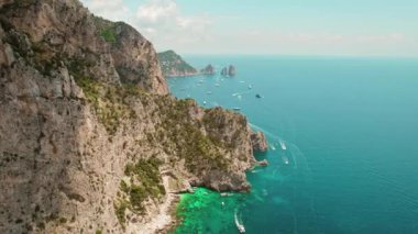 Capri Adası 'nın manzaralı manzarasında turkuaz deniz, kayıklar ve kayalıklarla gösteriliyor. Arka planda Faraglioni yığın..