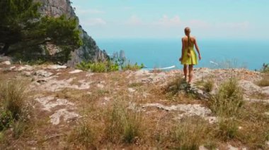 Uçurumun kenarından zümrüt deniz suyuyla Capri Adası 'na hayran bir kadın. Yalnız bir gezgin ünlü Faraglioni kaya oluşumlarına bakıyor...