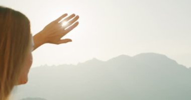 Bir kadın gözlerini güneşten korur, puslu dağlara bakar. Jest, etrafındaki manzaranın sıcaklığını ve parlaklığını yakalıyor...