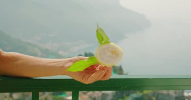 Limon dilimli dondurma, Balkon korkuluğunda, ötesindeki Misty Mountains ile. Bir el kesilmiş bir limon sunar, arka planda doğa...
