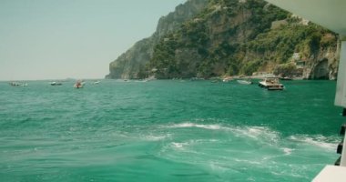 İtalya 'nın Positano kasabasında güneşli yaz güneşinin altında yüzen tekneleriyle Amalfi kıyısının kristal mavi deniz suları...
