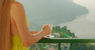 Kupadan çay içen, güneşli yaz gününde İtalya 'da Amalfi sahiline bakan bir kadın. Sahil manzarasına bakarken bir bayan sıcak bir içecek yudumluyor...