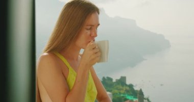 Uluslararası Kahve Günü. Rahatlatıcı bir ortamda kahvesini yudumlarken, kadın uzak bir ufka bakıyor. Sabah ışıkları balkonu aydınlatıyor...