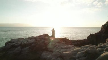 İspanya 'nın Tenerife kentindeki Los Gigantes uçurumlarındaki kayalık sahil şeridinde güneş okyanusun üzerinde batarken bir çift birbirine yakın duruyor...