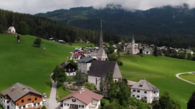 Avusturya 'daki Gosau köyünün büyüleyici bir manzarası var. Puslu dağların altındaki yemyeşil tepeleri süsleyen kilise ve antika binaları var...