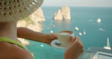 Kadınlar, yaz tatilleri sırasında Capri İtalya 'da bir balkondan dünyaca ünlü Faraglioni kayalıklarına ve denize bakarken kahve içerler...