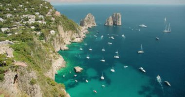 Capri Adası 'nın dramatik uçurumları, Faraglioni kayaları ve parlak bir yaz gününde derin mavi denizi noktalayan tekneleriyle süpürülen hava görüntüleri...