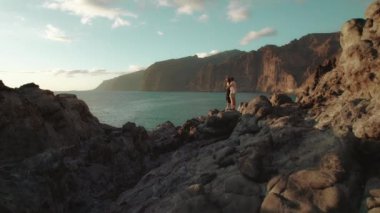 Çift, Tenerife 'deki Los Gigantes Kayalıkları' nın kayalık kıyı şeridinde, parlak mavi gökyüzünün altında okyanusu seyrediyor...