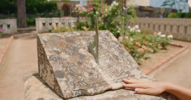Tarihi bir bahçedeki güneş saati cücesini işaret eden parmaklar taşın üzerine keskin bir gölge bırakır. Modern teknolojiden önce kullanılan zaman tutma yöntemleri..