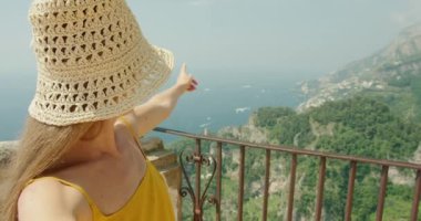 Bir kadın blogcu kameraya bakar ve sosyal ağ için bir video eleştirisi kaydeder. Arka planda Akdeniz olan bir balkonda turist..