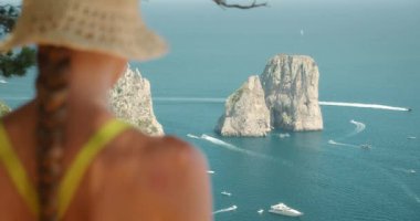 Hasır şapkalı kadın haritayı tutuyor ve açık bir günde İtalya 'nın Capri şehrinde gölgeli bir perspektiften Faraglioni kayalarına bakıyor...