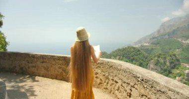 Kadın, arka planda deniz manzarası olan bir uçurumdan Amalfi Sahili 'ne bakan bir harita okuyor...