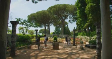 Turistler İtalya 'nın Ravello şehrinde uzun ağaçların altında yemyeşil bir gül bahçesini keşfediyorlar...