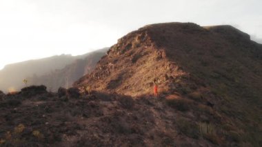 Sisli bir gün batımının altında kayalık bir dağ yamacında koşan kişi Tenerife, Kanarya Adaları 'nın engebeli arazisini ve kurak manzarasını gözler önüne seriyor...