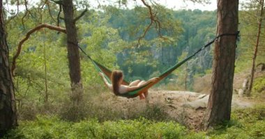 Almanya, Sakson İsviçre 'de kayalık uçurumları olan gür bir ormandaki hamakta dinlenen bir kadın, sakin yaz ortamının tadını çıkarıyor...