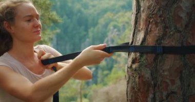 Bir kadının eli, çam ağacının gövdesine sıkı bir hamak kayışı çekiyor, yemyeşil bir orman zeminine kurulmuş...