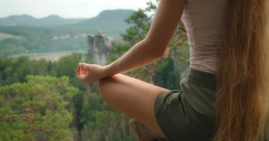 Arka planda güzel bir orman manzarası olan uçurumda meditasyon yapan bir kadının yakın çekimi...