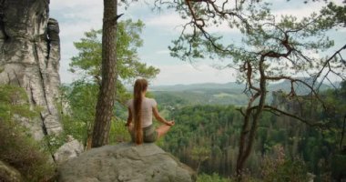 Yazın çam ağacı ormanı olan yeşil vadileri ve uzak tepeleri gören bir kayanın üzerinde meditasyon yapan bir kadın..